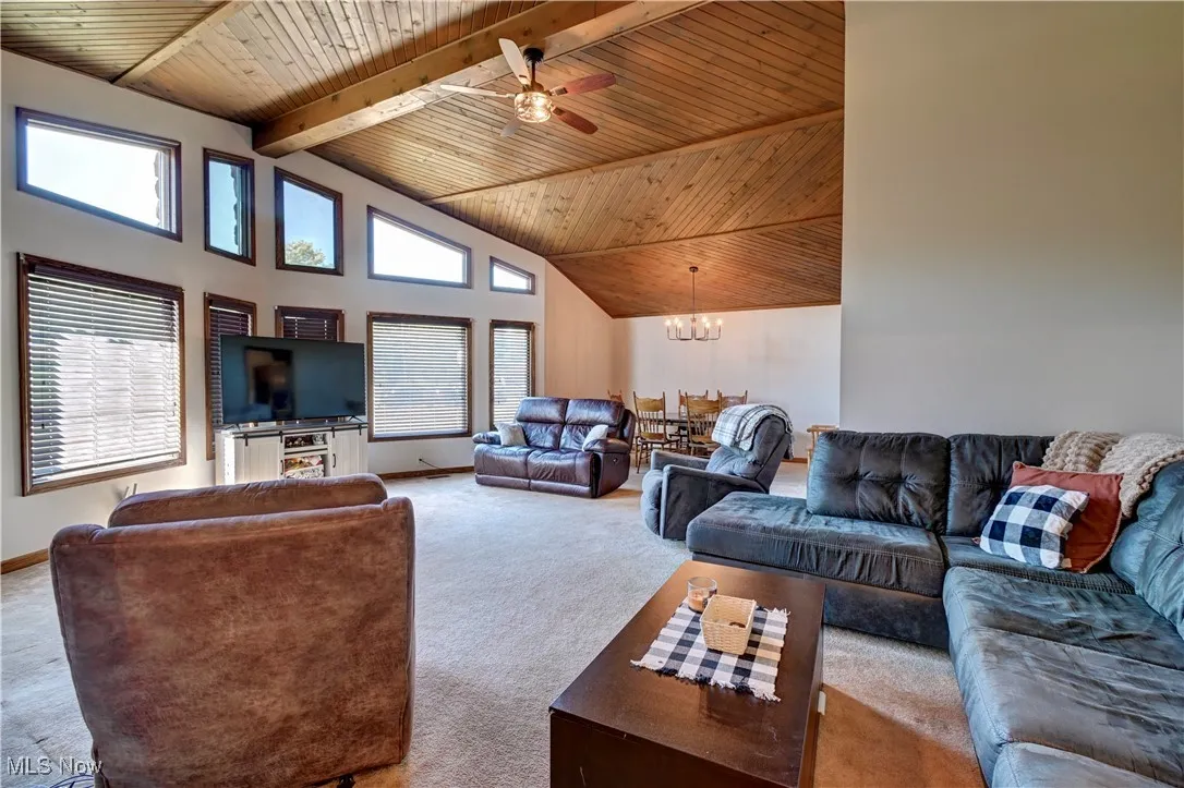 Living room with high vaulted ceiling, carpet floors, a ceiling fan, a wooden ceiling with exposed beams, and a chandelier