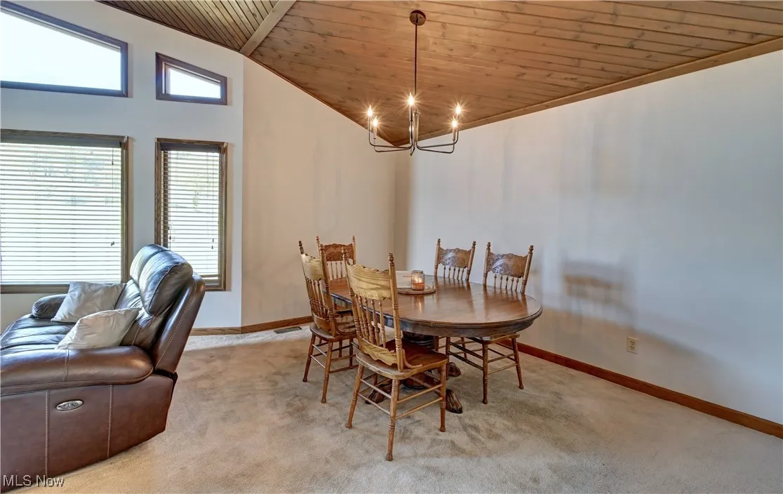 Carpeted dining area with wood ceiling, a chandelier, and high vaulted ceiling