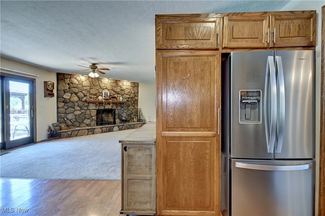 Kitchen with stainless steel fridge with ice dispenser, light wood-type flooring, a textured ceiling, brown cabinets, and a fireplace