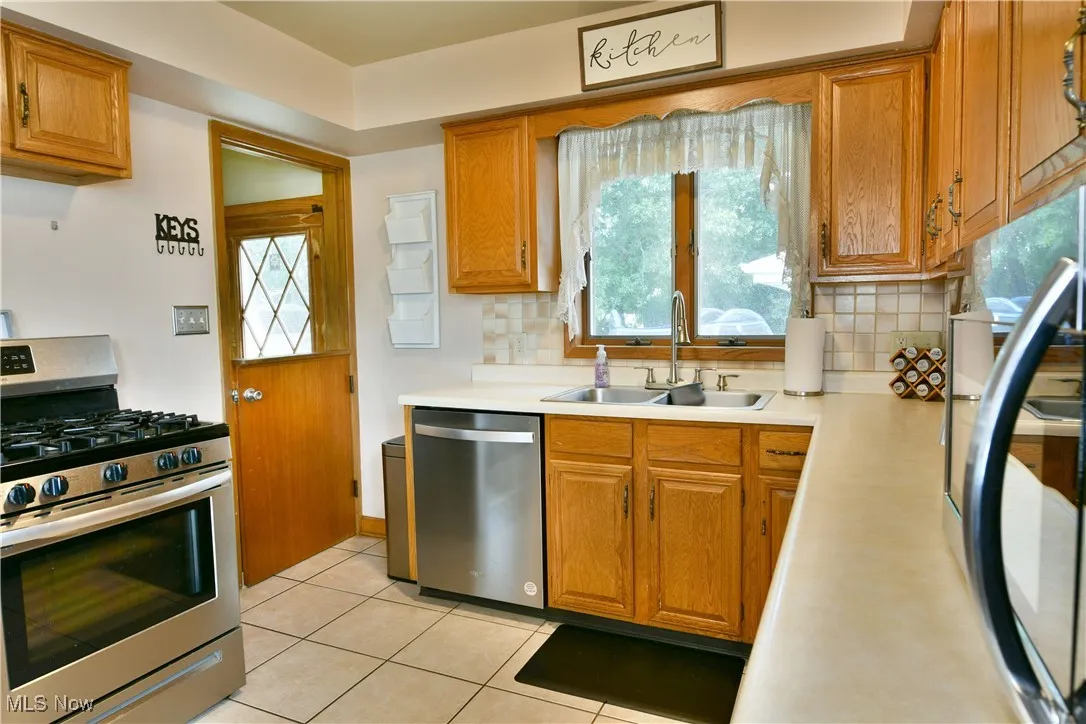 Kitchen with stainless steel appliances, brown cabinetry, backsplash, light countertops, and plenty of natural light