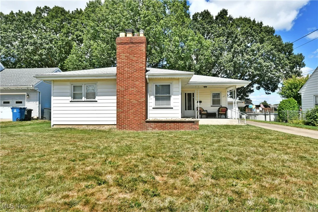 Front of house featuring covered porch, a yard, a chimney, and driveway