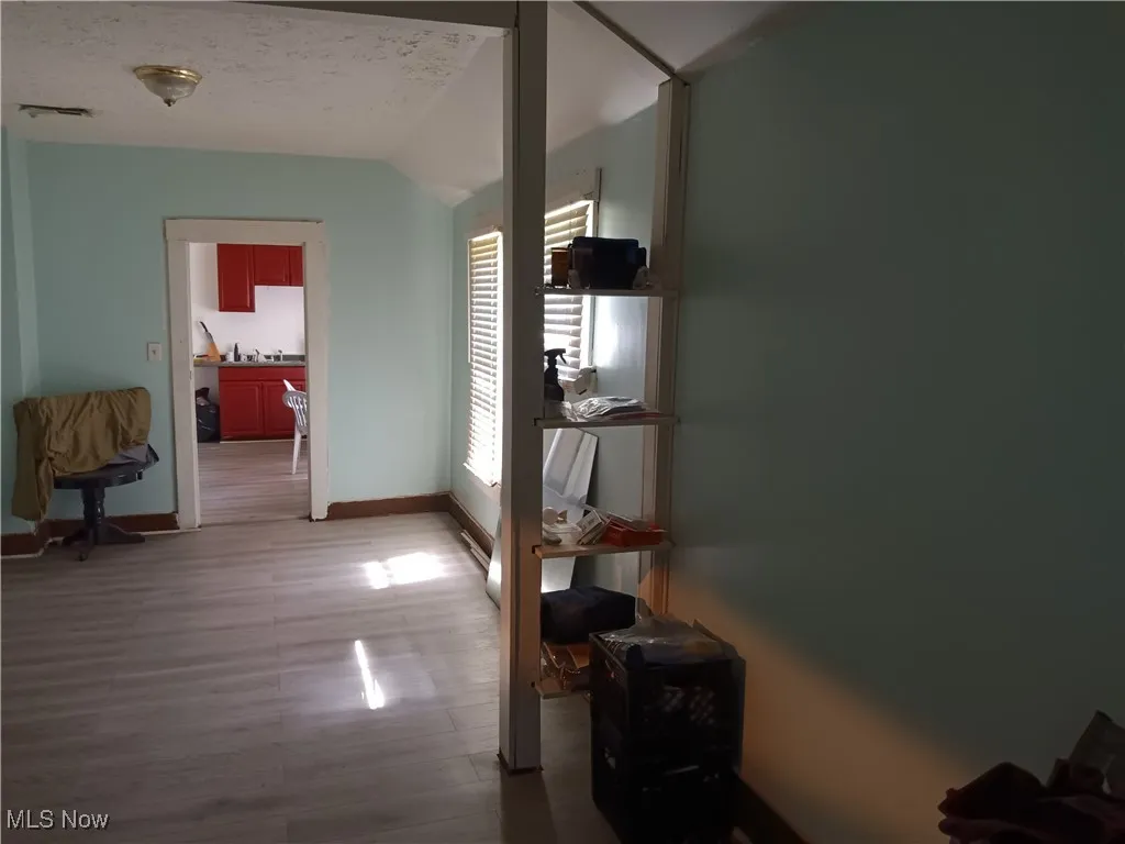 Corridor featuring light wood-style floors, a textured ceiling, and lofted ceiling