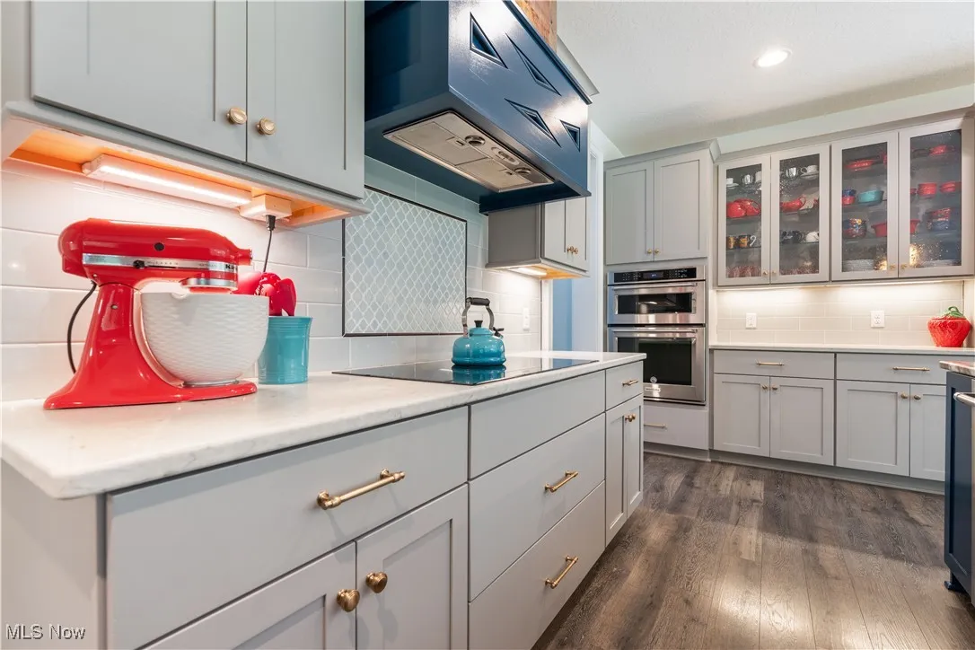 Kitchen featuring custom range hood/cooktop, a tasteful backsplash, glass insert cabinets, and a wall oven.