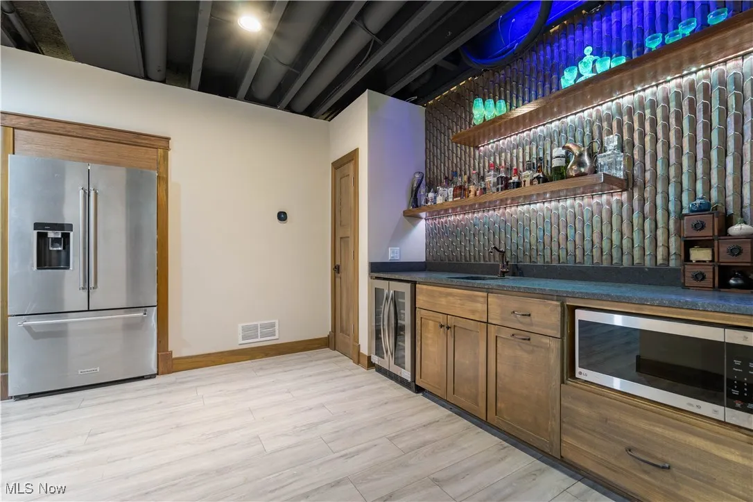 Lower level  bar with stainless steel appliances, open shelves, and a wine cooler.