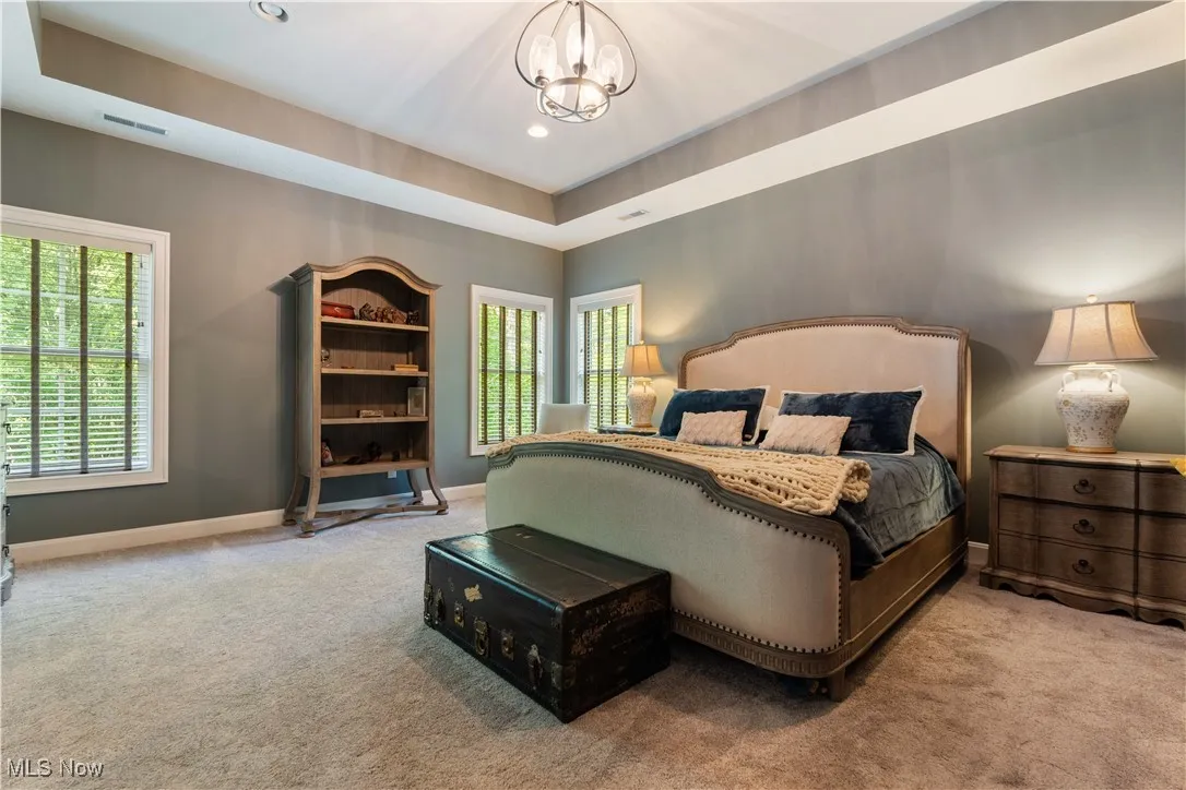Carpeted master suite featuring a tray ceiling with recessed lighting, and a  chandelier.