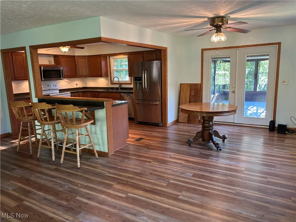 Kitchen featuring a ceiling fan, stainless steel appliances that stay with purchase, brown cabinetry, and new vinyl flooring - open concept kitchen, dining, living room