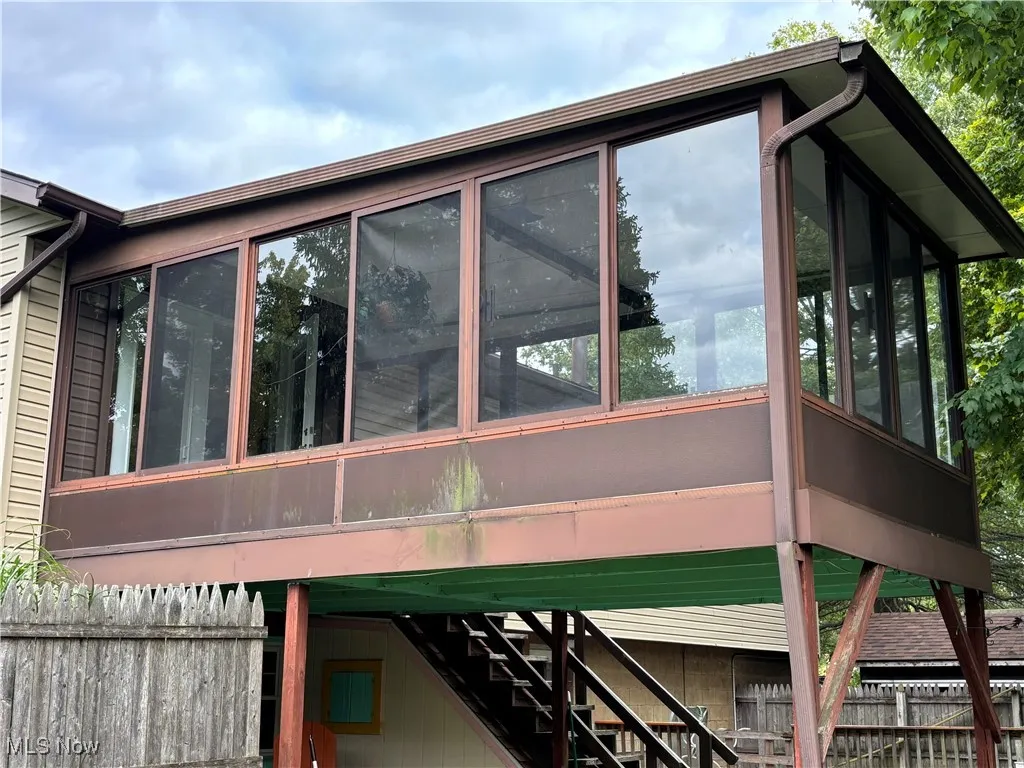 View of property exterior with stairway, a sunroom, and a wooden deck
