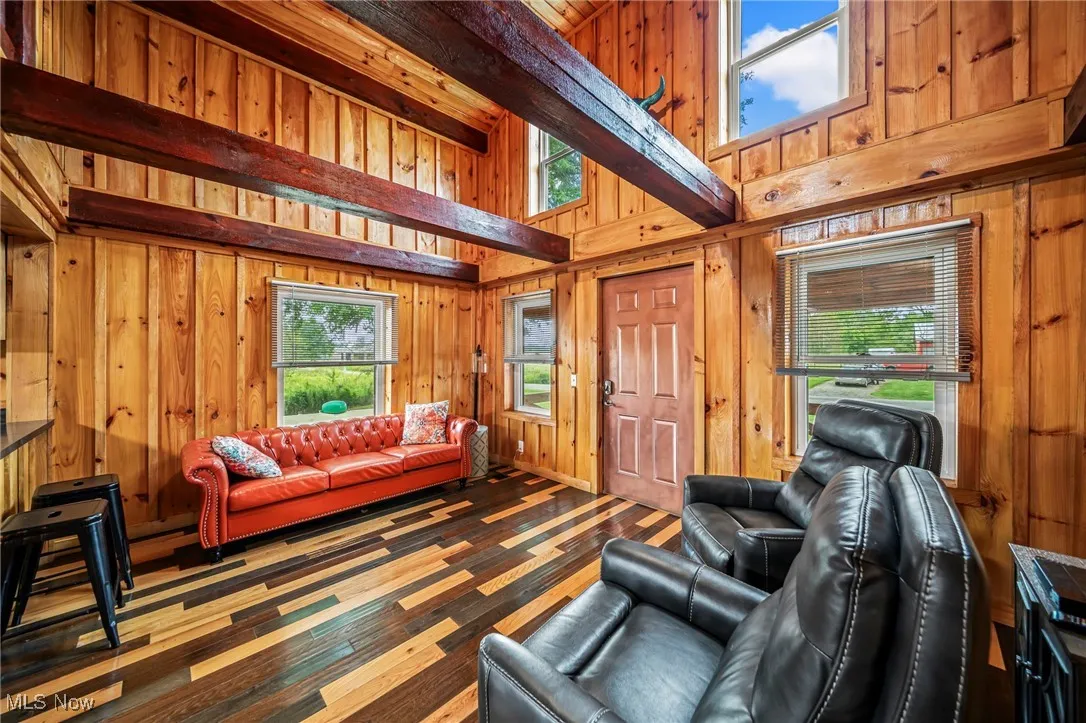 Living room with a towering ceiling, beamed ceiling, wood walls, and wood finished floors