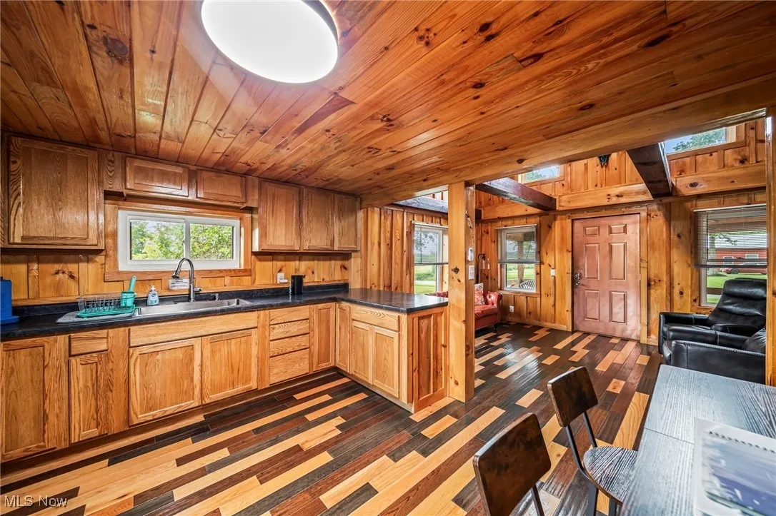 Kitchen with a peninsula, wood walls, dark countertops, wood ceiling, and brown cabinets