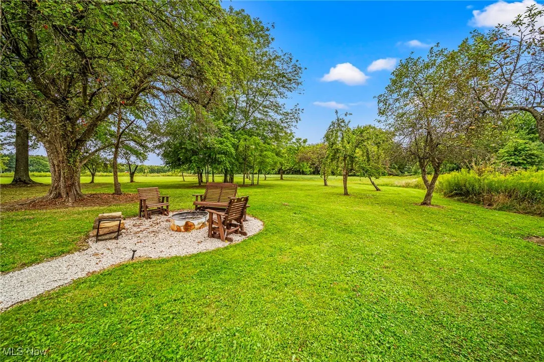 View of grassy yard featuring a patio area, a fire pit, and view of scattered trees