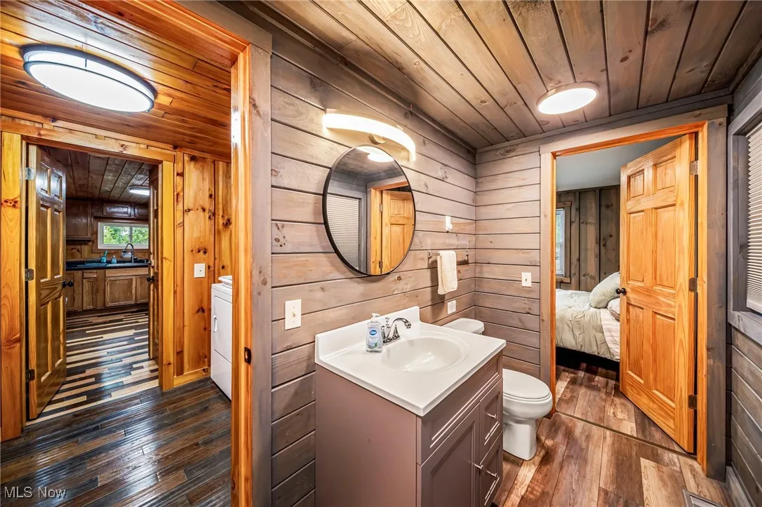 Bathroom with wooden ceiling, dark wood finished floors, vanity, wood walls, and ensuite bath