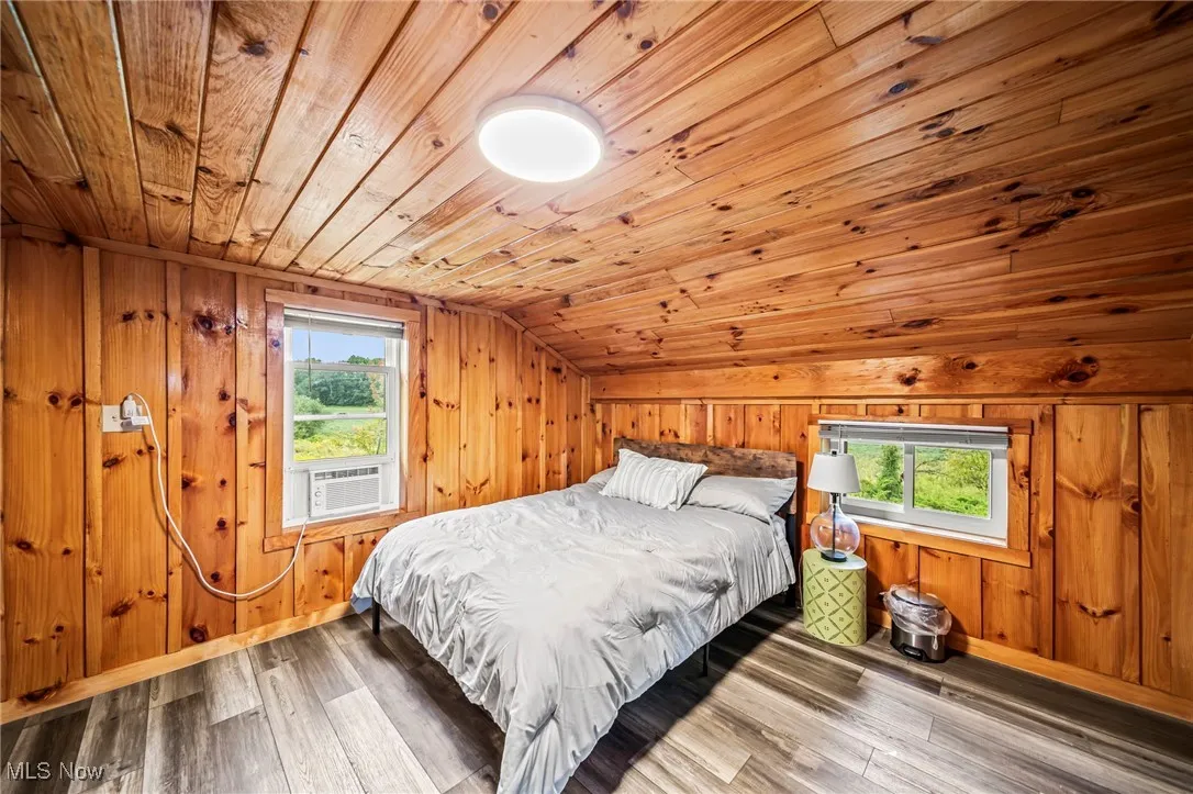 Bedroom with vaulted ceiling, wood walls, wooden ceiling, wood finished floors, and cooling unit
