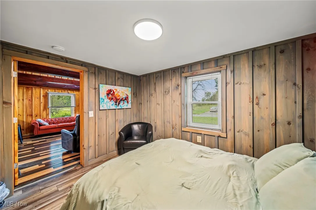 Bedroom with wood finished floors, multiple windows, and wooden walls