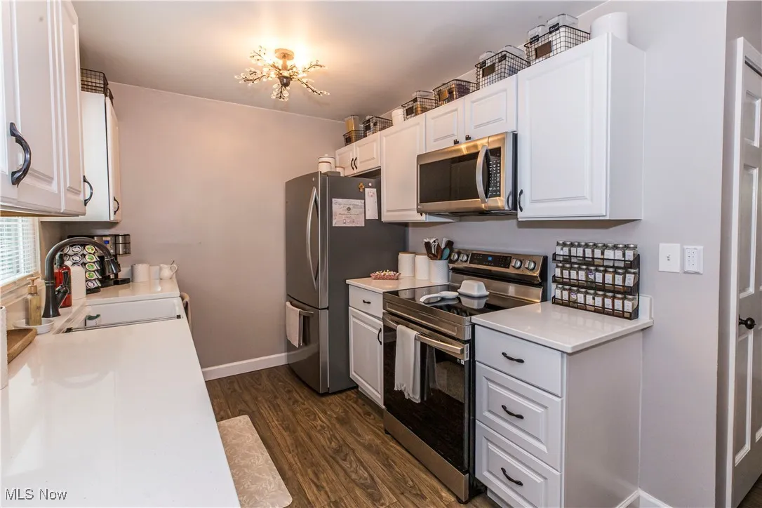 Kitchen featuring stainless steel appliances, dark wood finished floors, white cabinetry, and light stone counters
