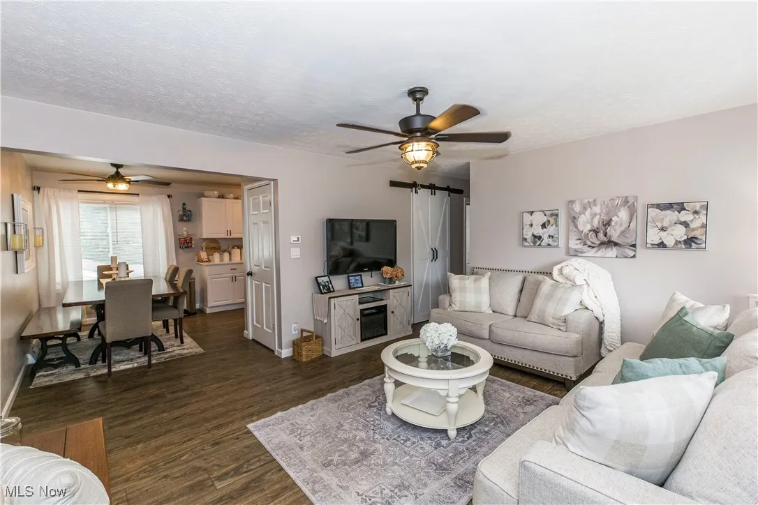Living room featuring a ceiling fan, a barn door, dark wood-type flooring, and a textured ceiling