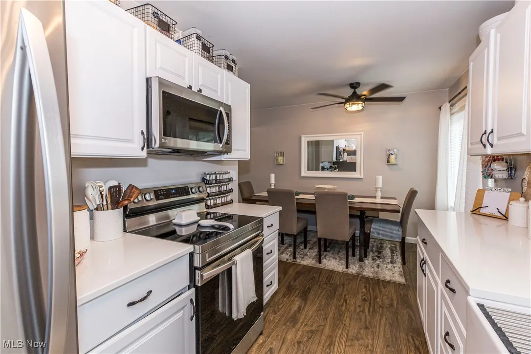 Kitchen featuring appliances with stainless steel finishes, dark wood-type flooring, white cabinetry, ceiling fan, and light stone counters