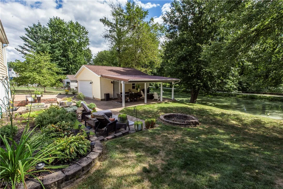 View of grassy yard featuring an outdoor fire pit, a patio, an outbuilding, a garage, and a water view