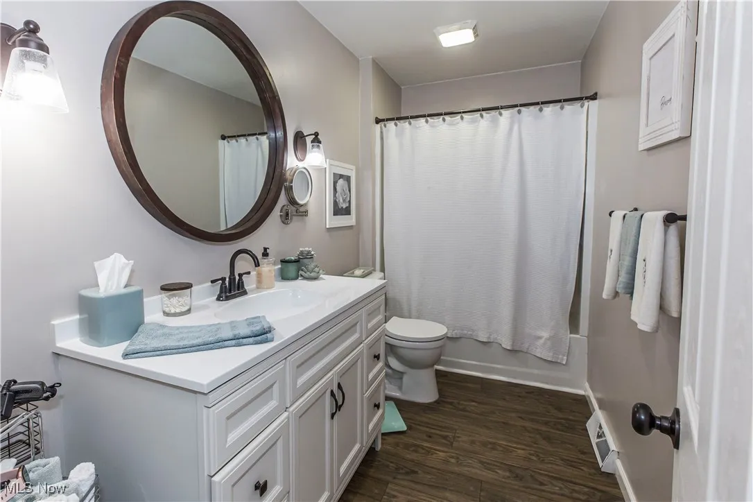 Bathroom featuring dark wood-type flooring, vanity, and shower / bath combination with curtain