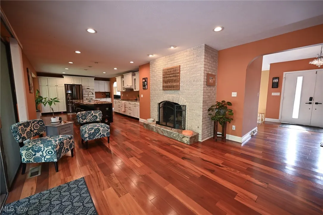 Living room with recessed lighting, dark wood-type flooring, a brick fireplace, and arched walkways