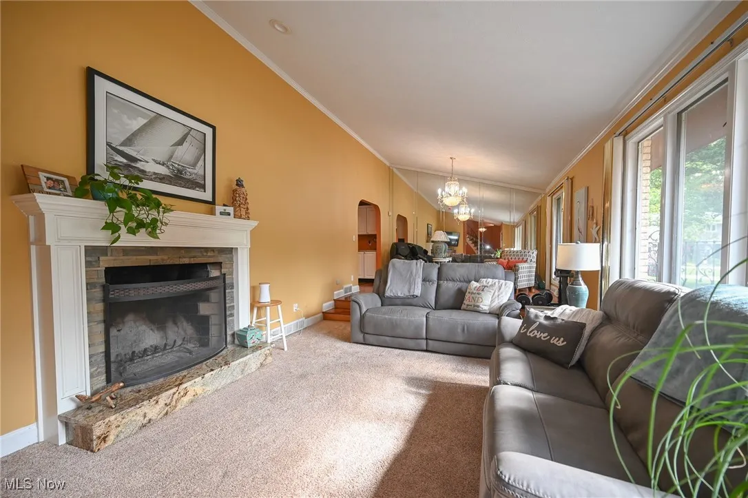 Carpeted living area featuring crown molding, arched walkways, a fireplace with raised hearth, and a chandelier