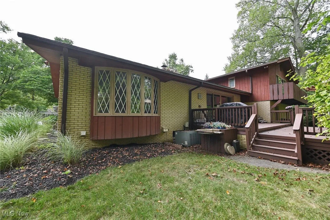 Back of property featuring brick siding, a wooden deck, and a yard