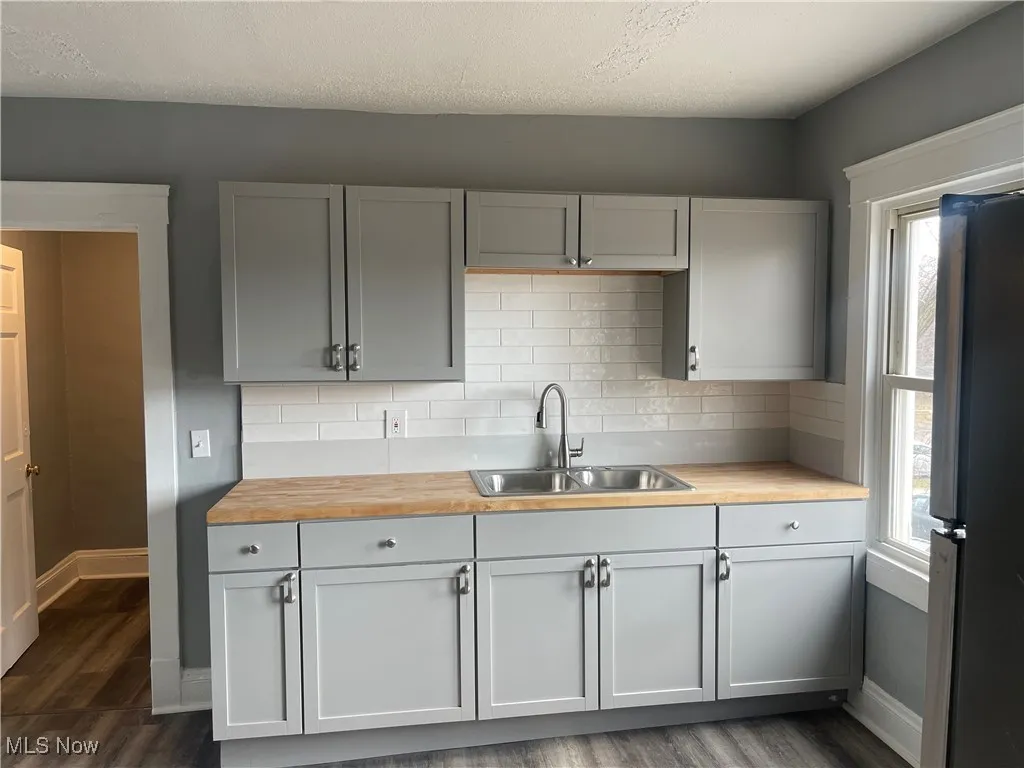 Kitchen with tasteful backsplash, butcher block counters, freestanding refrigerator, dark wood-style floors, and gray cabinets