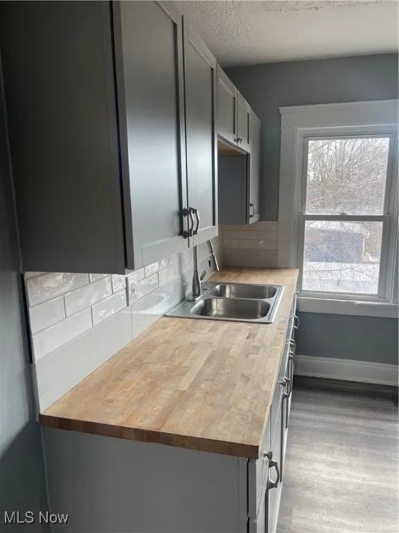 Kitchen with tasteful backsplash, gray cabinetry, butcher block countertops, a textured ceiling, and dark wood-style floors