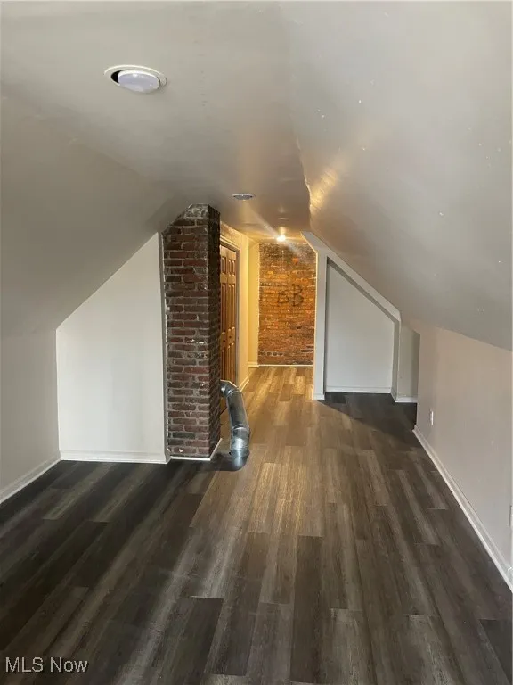 Bonus room featuring brick wall, lofted ceiling, and dark wood-style flooring