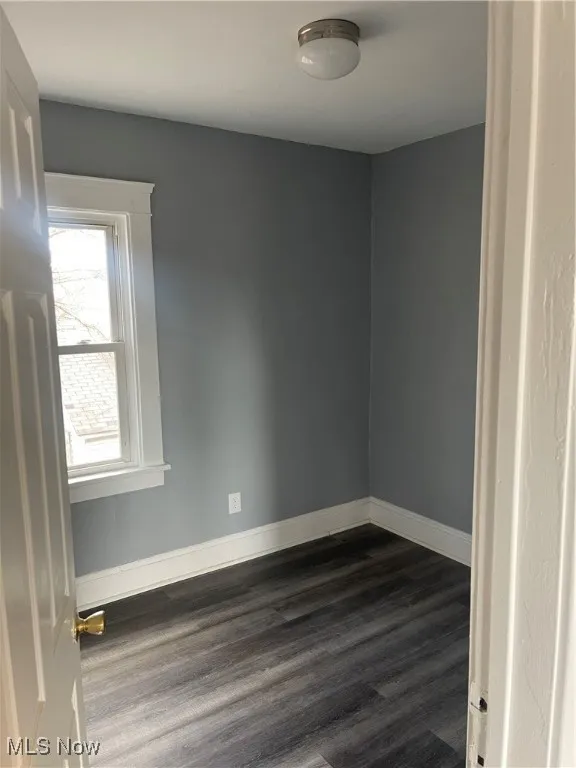 Empty room with dark wood-type flooring and baseboards
