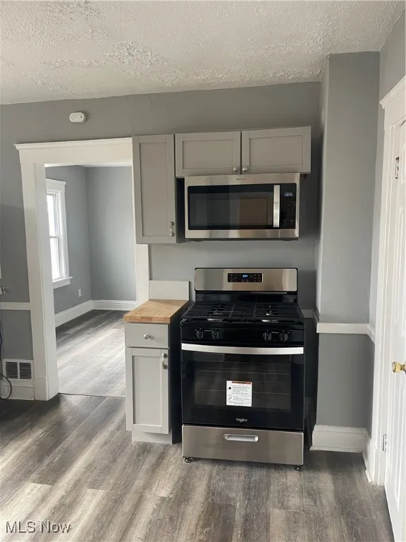 Kitchen featuring range, gray cabinets, a textured ceiling, stainless steel microwave, and dark wood-style floors