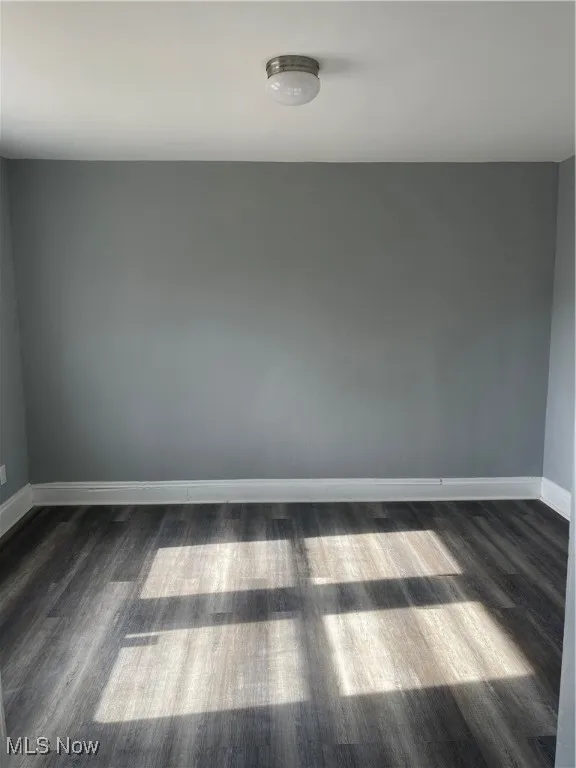 Spare room featuring baseboards and dark wood-style floors