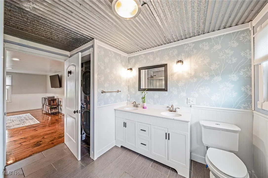 Bathroom with a wainscoted wall, double vanity, light wood finished floors, and wallpapered walls