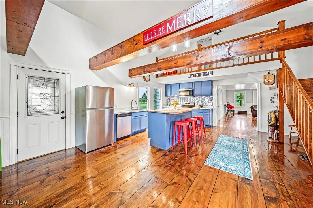 Kitchen featuring beam ceiling, blue cabinetry, stainless steel appliances, dark wood-style flooring, and a breakfast bar area