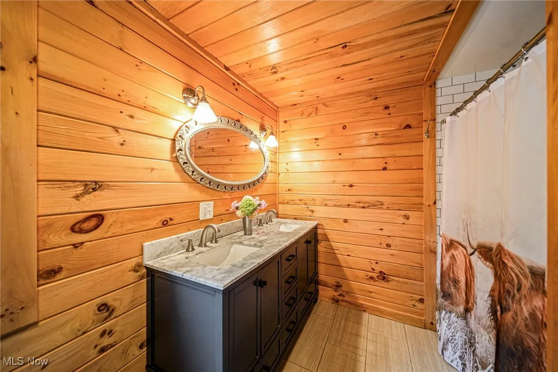 Full bath featuring wooden walls, double vanity, wood ceiling, and a shower with shower curtain