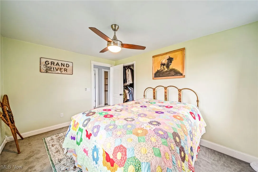 Bedroom with a walk in closet, a ceiling fan, and light colored carpet