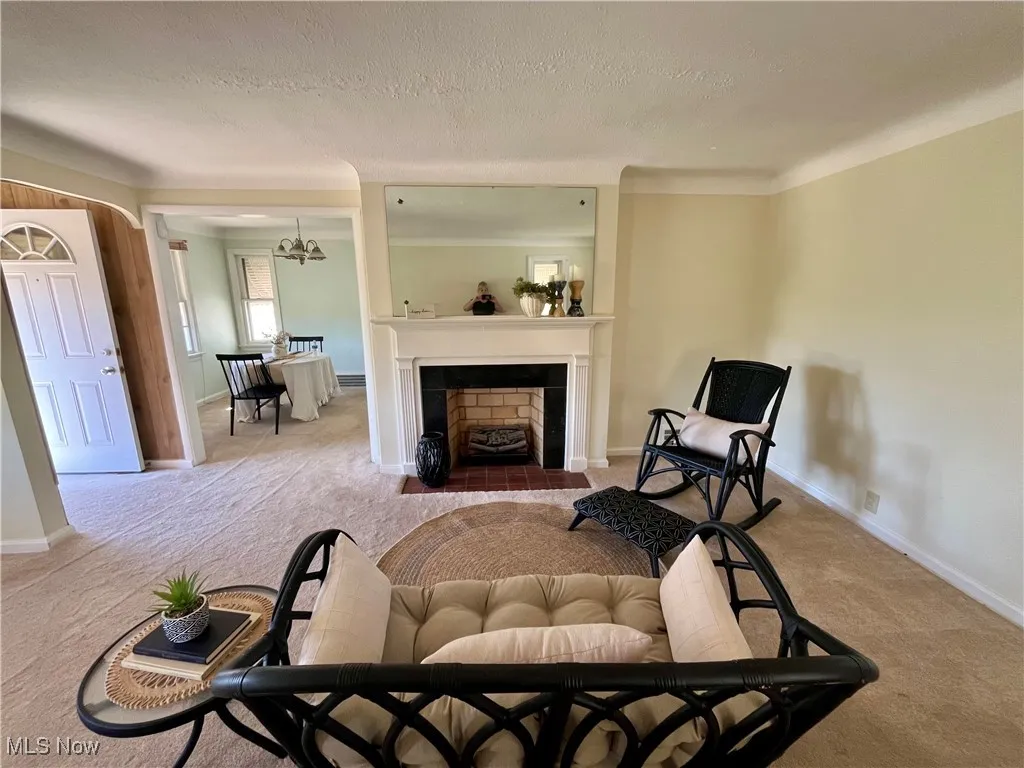 Living area featuring a textured ceiling, carpet floors, a fireplace with flush hearth, and a chandelier