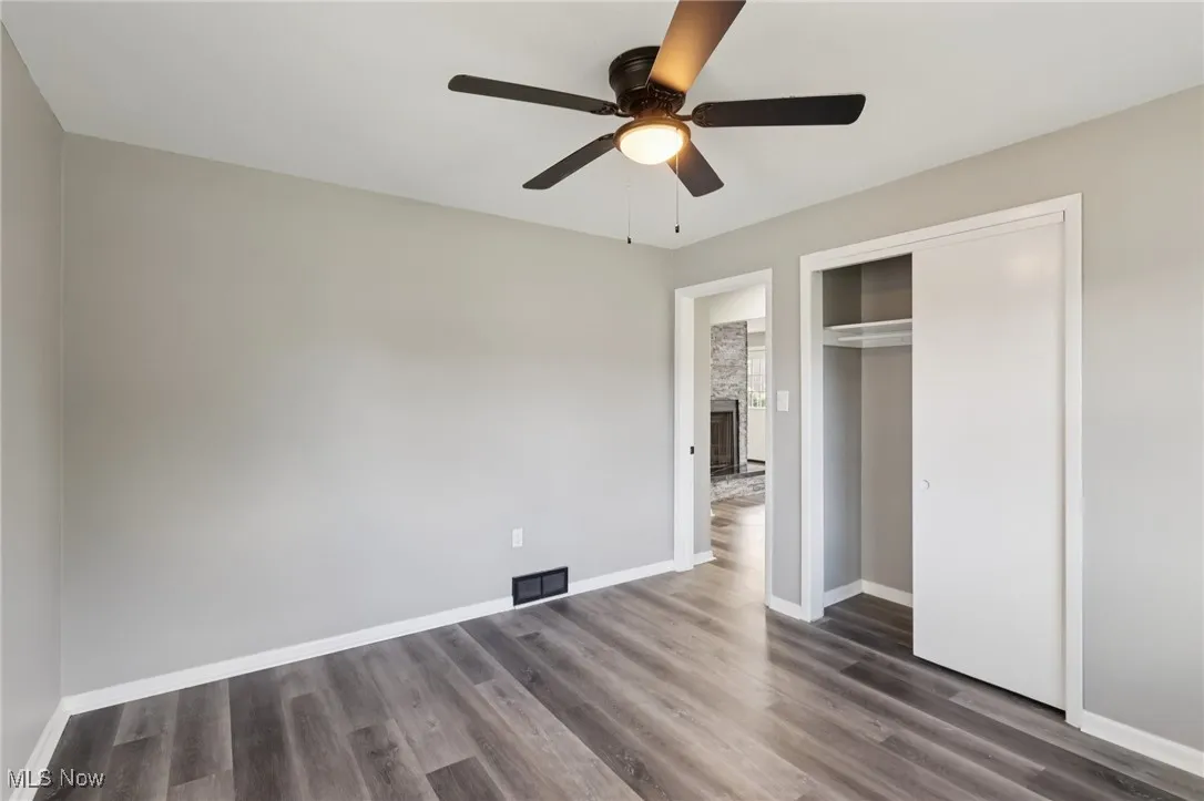 Unfurnished bedroom with dark wood-style floors, a closet, ceiling fan, and a large fireplace