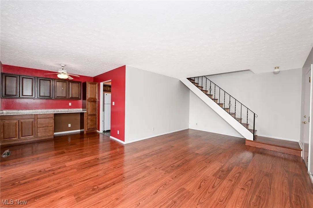 Living room featuring a textured ceiling, dark wood-type flooring, stairway, built in desk, and ceiling fan