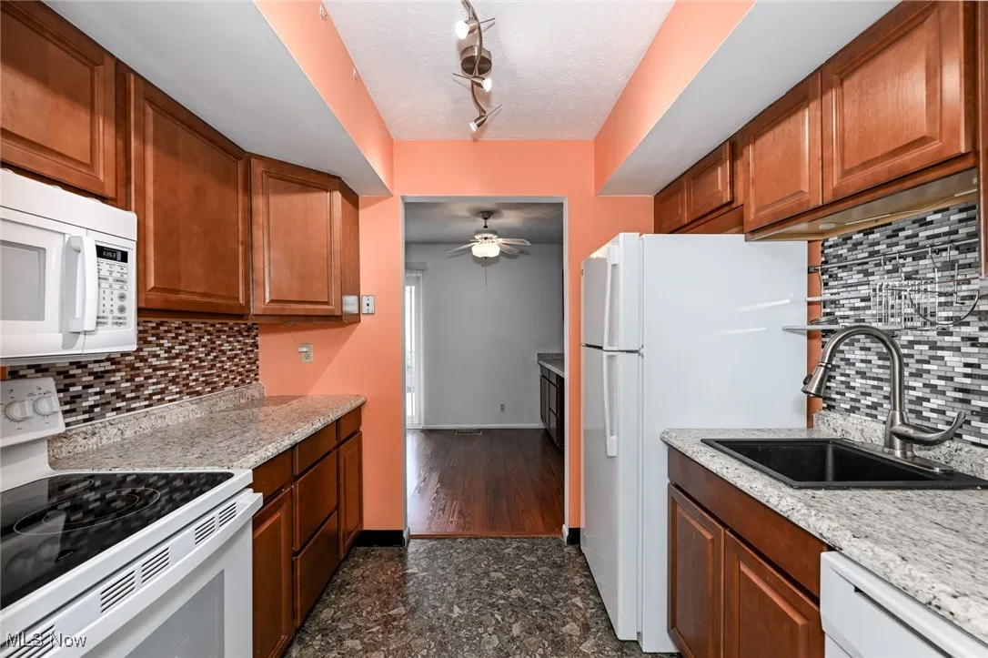 Kitchen featuring backsplash, white appliances, light counters, & brown cabinetry