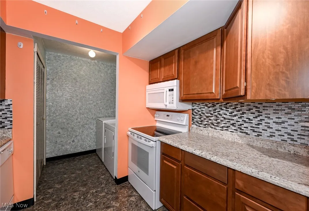 Kitchen with backsplash, white appliances, brown cabinets, separate washer and dryer, and light countertops