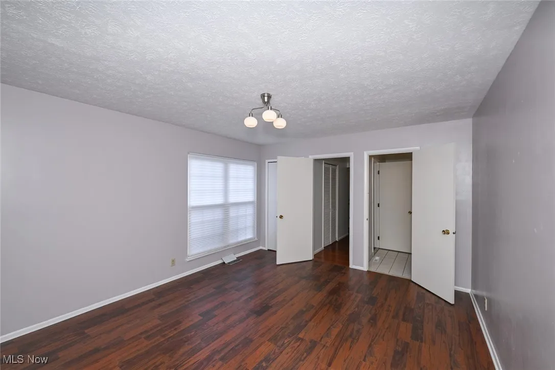 Main level primary bedroom #1 featuring dark wood finished floors, a textured ceiling, closet and ensuite