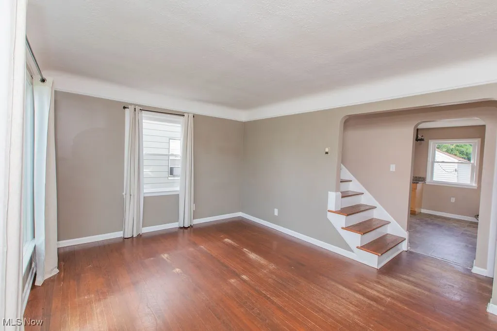 Empty room featuring dark wood-style flooring, arched walkways, stairway, and a textured ceiling