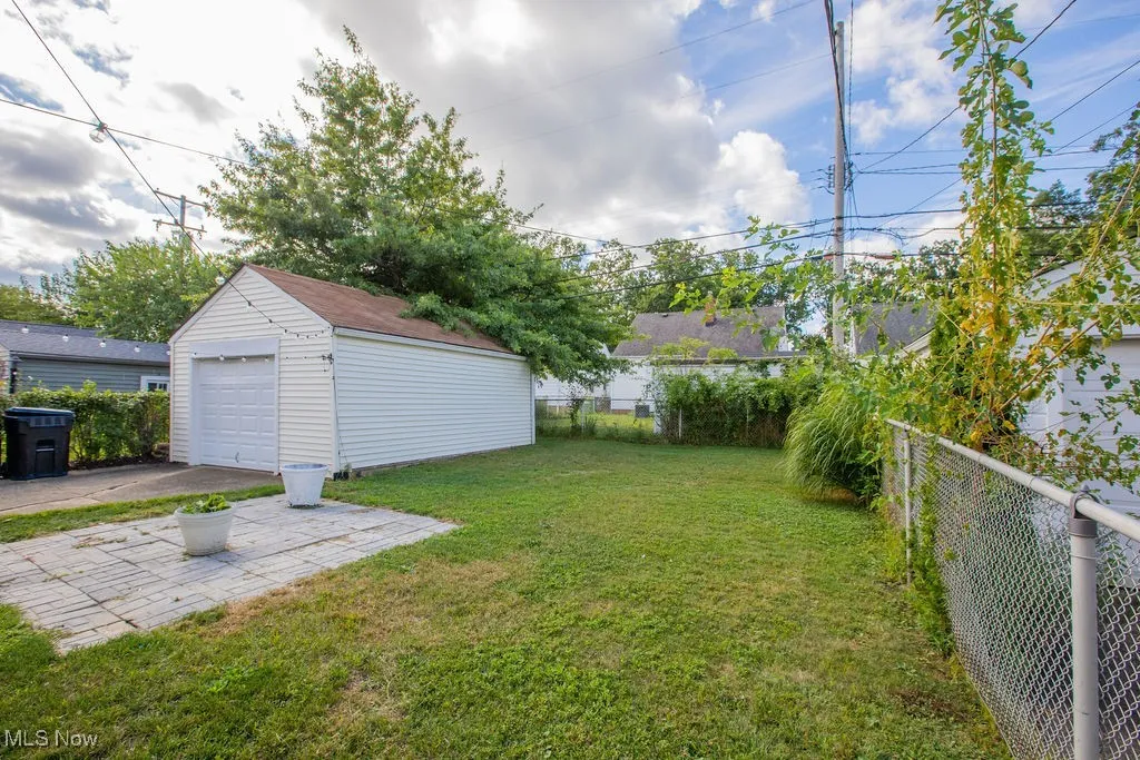 Fenced backyard with an outbuilding, a detached garage, a patio, and driveway