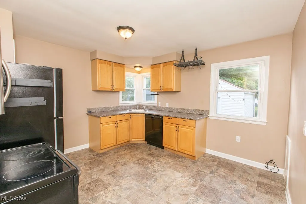 Kitchen featuring range with electric cooktop, light brown cabinetry, black dishwasher, stainless steel fridge, and stone finish floors