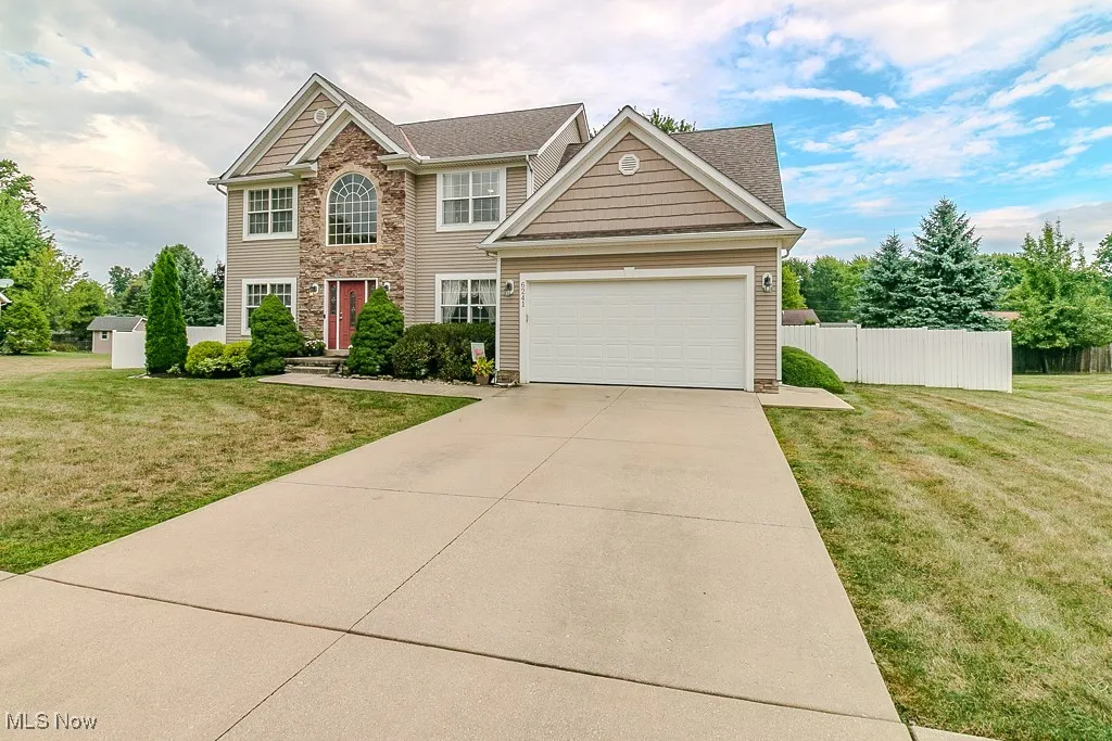 Colonial home featuring stone siding, driveway, an attached garage, and roof with shingles