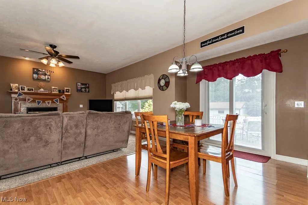 Dining room featuring light wood finished floors, a chandelier, a fireplace, and a ceiling fan