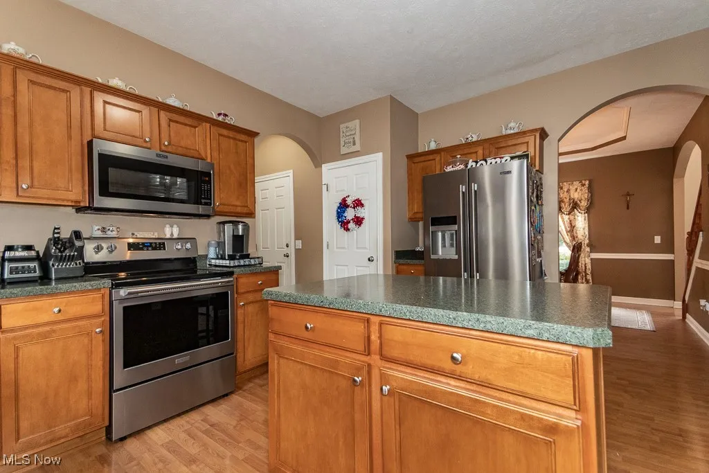 Kitchen featuring arched walkways, brown cabinets, stainless steel appliances, a kitchen island, and light wood-style floors