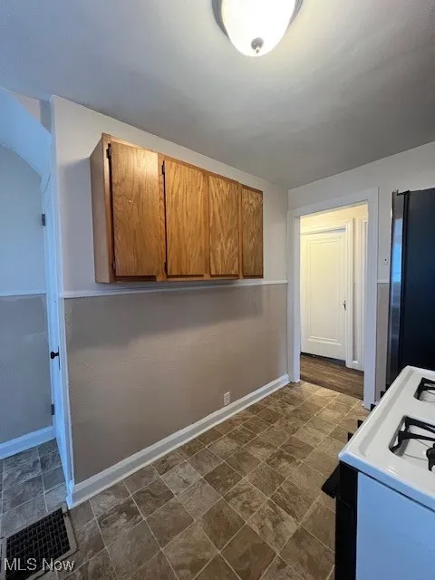 Kitchen featuring brown cabinetry, range, stone finish flooring, refrigerator, and light countertops