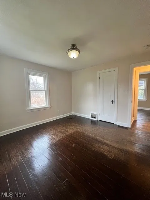 Empty room with dark wood-type flooring and baseboards