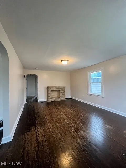 Unfurnished living room featuring arched walkways, dark wood-style floors, and a stone fireplace
